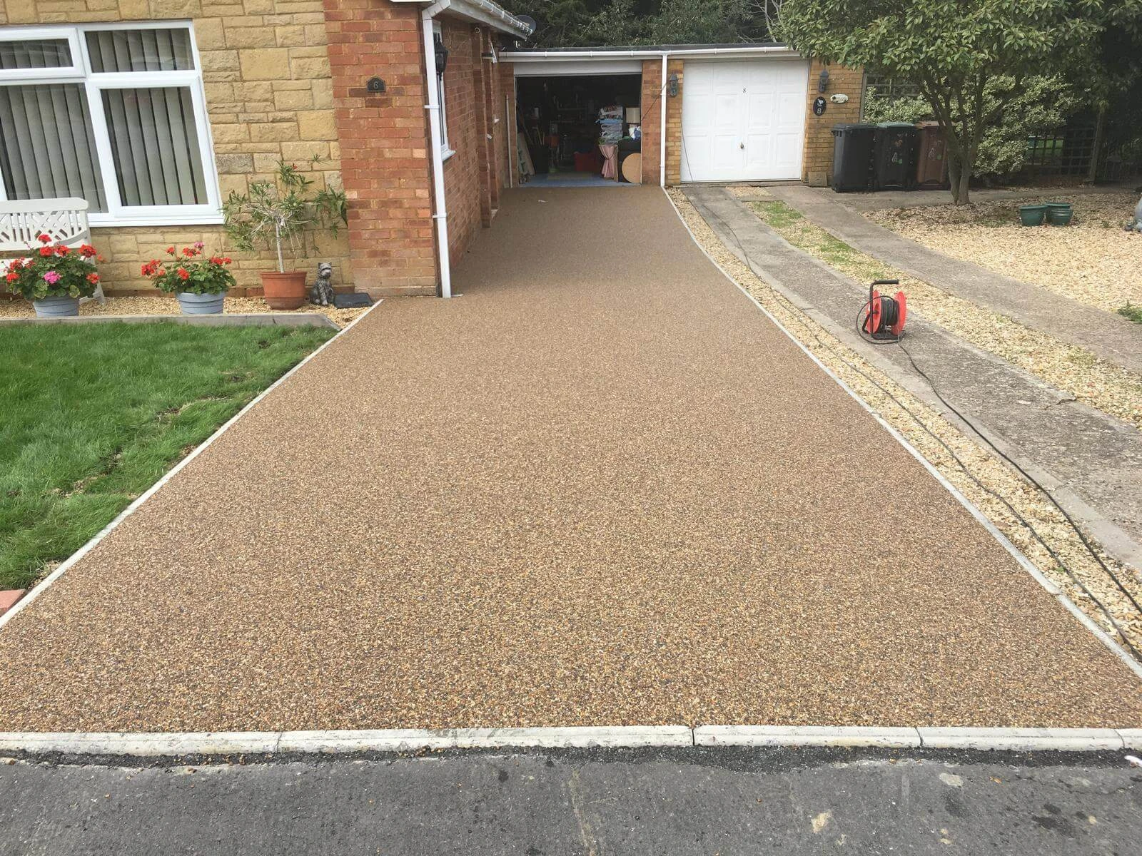 A newly laid resin driveway next to a house and leading to a double garage